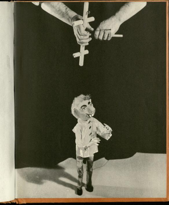 A very silly-looking marionette being pulled by a pair of hands pulling its strings.
